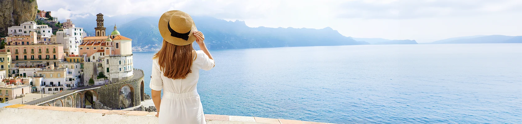 Tourisme en Italie. Vue de dos d'une jeune femme au chapeau de paille et en robe blanche avec village Atrani sur fond floral, côte d'Amalfi, Italie.