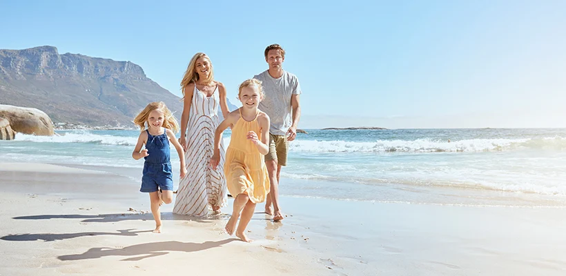 Jeune famille joyeuse avec deux enfants courant sur la plage et profitant des vacances d'été. Deux petites filles énergiques courent devant tandis que leur mère et leur père suivent en arrière-plan