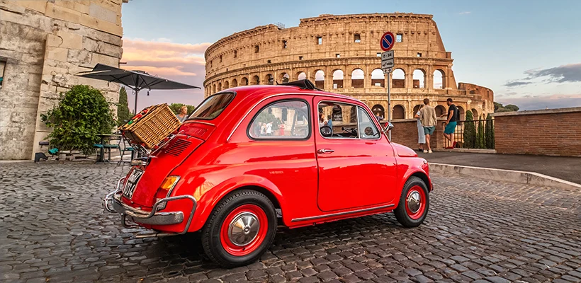 Petite Fiat 500 rouge devant le colisée au coucher du soleil avec un panier de pique-nique à l'arrière