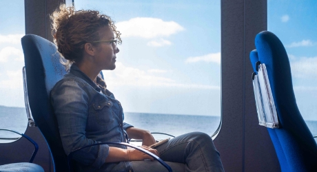 Salle espace fauteuils d’un des ferries de Moby Lines avec une passagère assise sur un fauteuil bleu regardant par la fenêtre le paysage qui défile