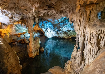 Une photo prise à l’intérieur des grottes de Neptune en Sardaigne, on aperçoit des stalagmites et un lac souterrain