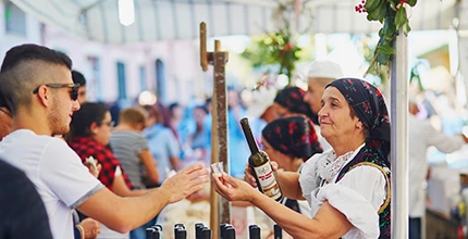 Une image sur laquelle on observe une femme en habit traditionnel sarde qui sert un verre un homme à l’occasion du festival Automne en Barbagia